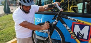 Bring your bike on MetroBus step 3: Man pulling and lifting the tire hook to secure it on top of the bike front tire. 