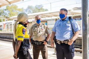 A Deputy Sheriff, Police Officer, and G4S Security contractor stand on the platform of the Delmar Loop MetroLink platform.