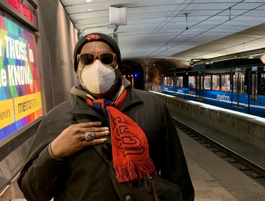 Passenger Rodney standing on the 8th and Pine platform looking at the camera with a blue MetroLink train behind him