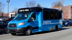 A Call-A-Ride van drives down a residential street. Red brick building appear in the background.