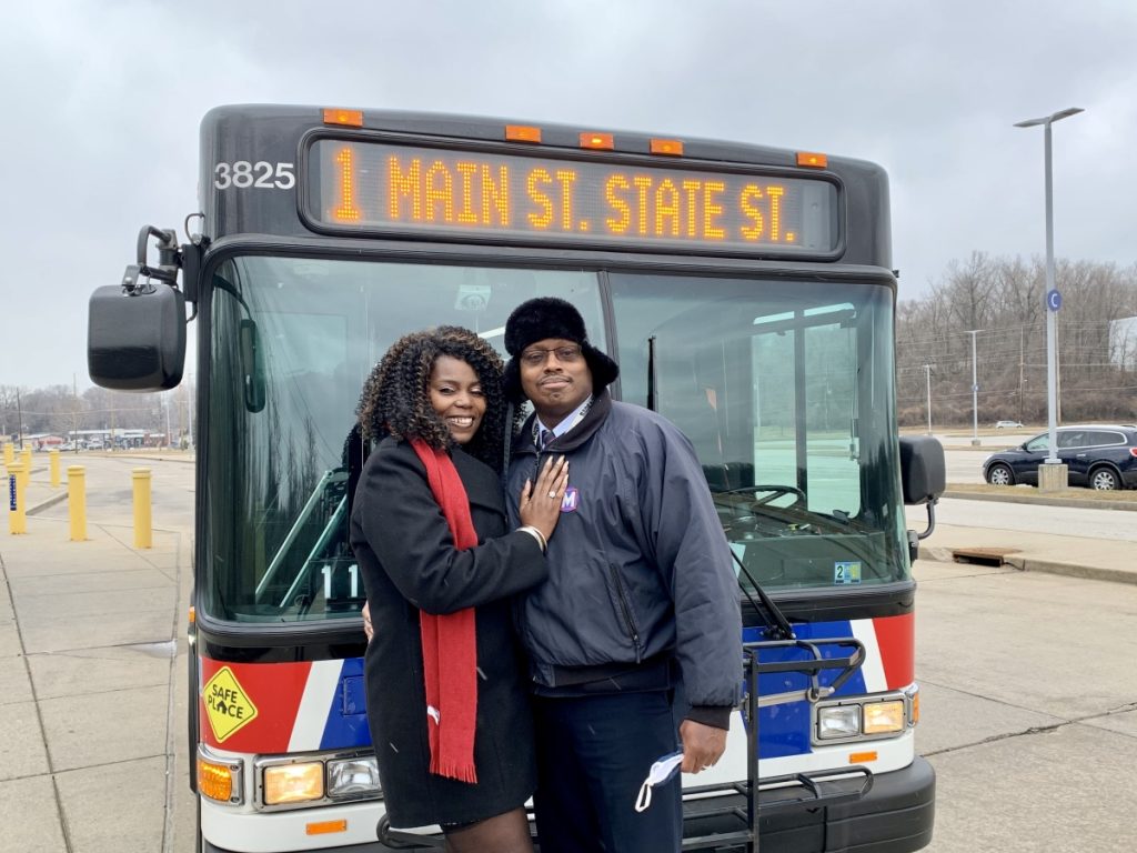 Passenger Profile: Lawanda and Jose standing in front of a MetroBus with a headsign that reads "1 Main St State St"