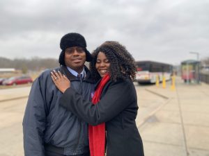 Passenger Profile: Lawanda and Jose standing near a bus bay, with the back of a MetroBus behind them. They are smiling, and she has her hand on his chest.