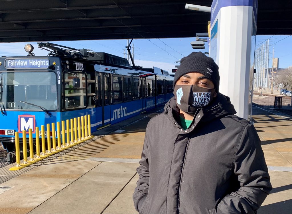 Passenger Robert standing on the Grand MetroLink Station platform looking at the camera, with a blue MetroLink train behind him