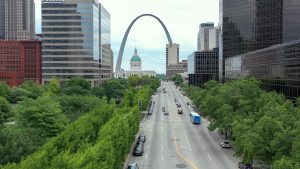 Aerial shot of a MetroBus driving down Market street downtown. Trees line market street and the Old Courthouse and Gateway Arch appear in the background.