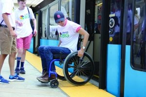 MetroLink passenger exiting a train onto the platform in a wheelchair. Passenger is wearing jeans, a whit shirt and blue baseball cap