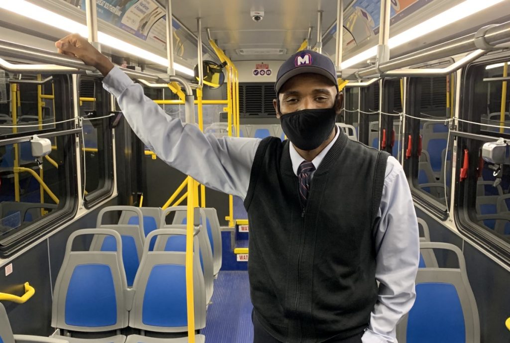 MetroBus Operator E'Quain standing on a bus looking at the camera and wearing a mask