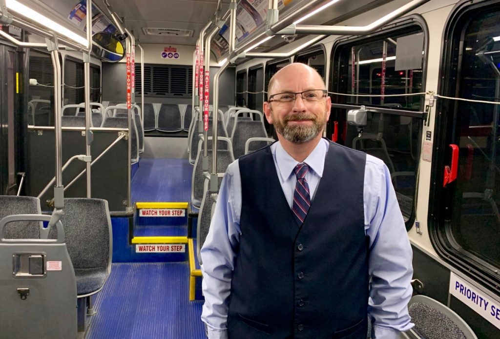 MetroBus Operator Ken standing on the inside of a bus, smiling at the camera