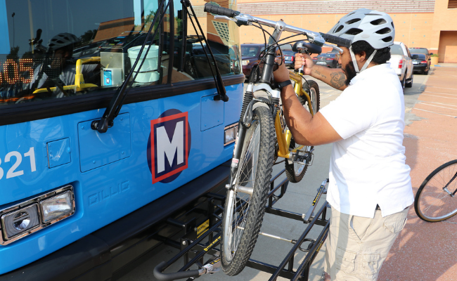 Bring your bike on MetroBus step 2: Man lifting up a bike to place the tires into the bike rack slots.