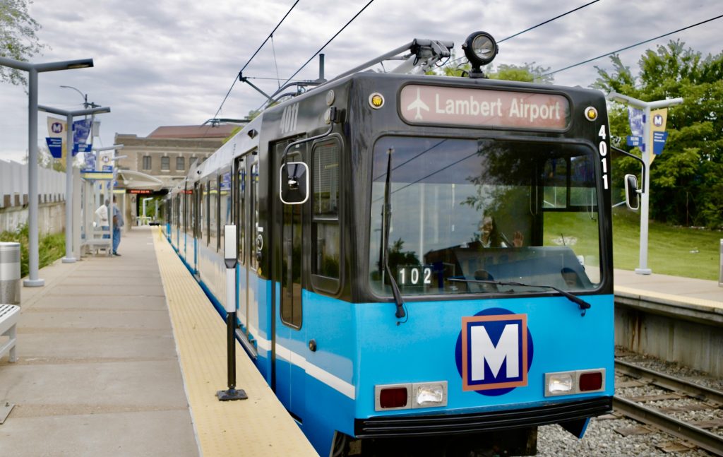 MetroLink train stopped at the platform of the Delmar Loop MetroLink station. Riders wait on the platform.