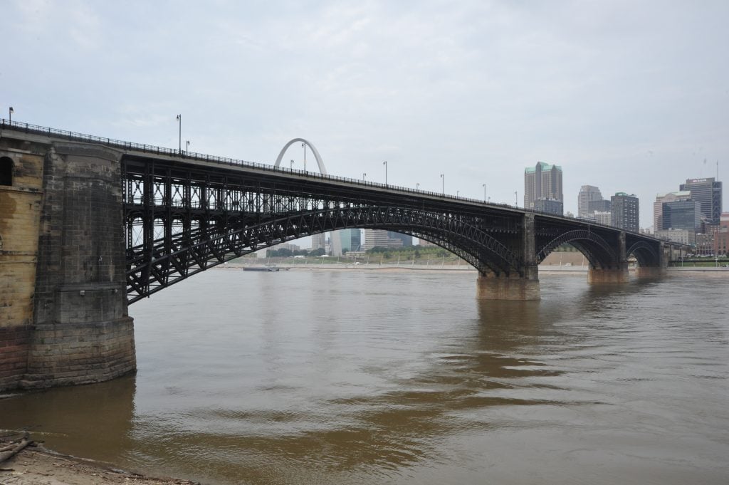 A sweeping view of the historic Eads Bridge spanning the Mississippi River with a background that includes the Gateway Arch and downtown St. Louis.