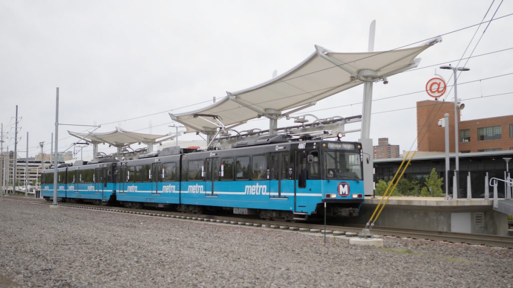 MetroLink train stopped at the Cortex MetroLink station. The canopy of the station and Cortex campus appear in the background.