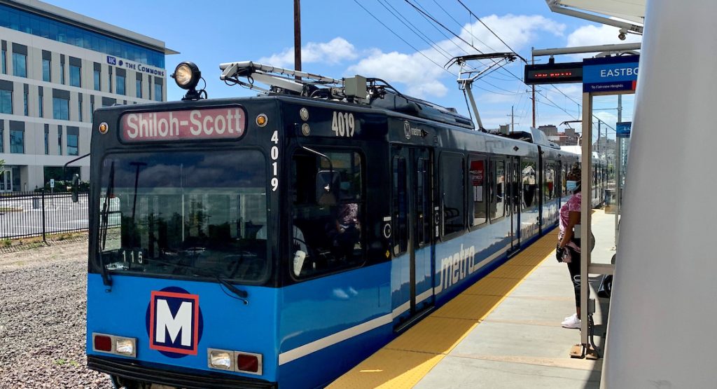 MetroLink train stopped at the platform of the Cortex MetroLink station. A rider wearing a mask stands on the platform.