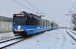 Front of a west-bound MetroLink train arriving at the North Hanley station. It is snowing and snow covers the ground and tracks.