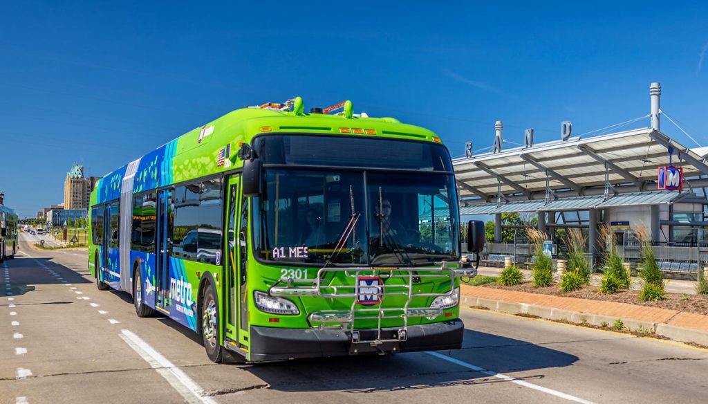 An articulated electric bus passing the Grand MetroLink Station and Scott Avenue Transit Plaza.