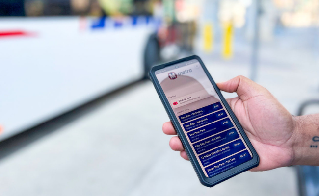 Image of a passenger holding their smartphone with the mobile fares in Transit app showing. A MetroBus is blurry in the background.