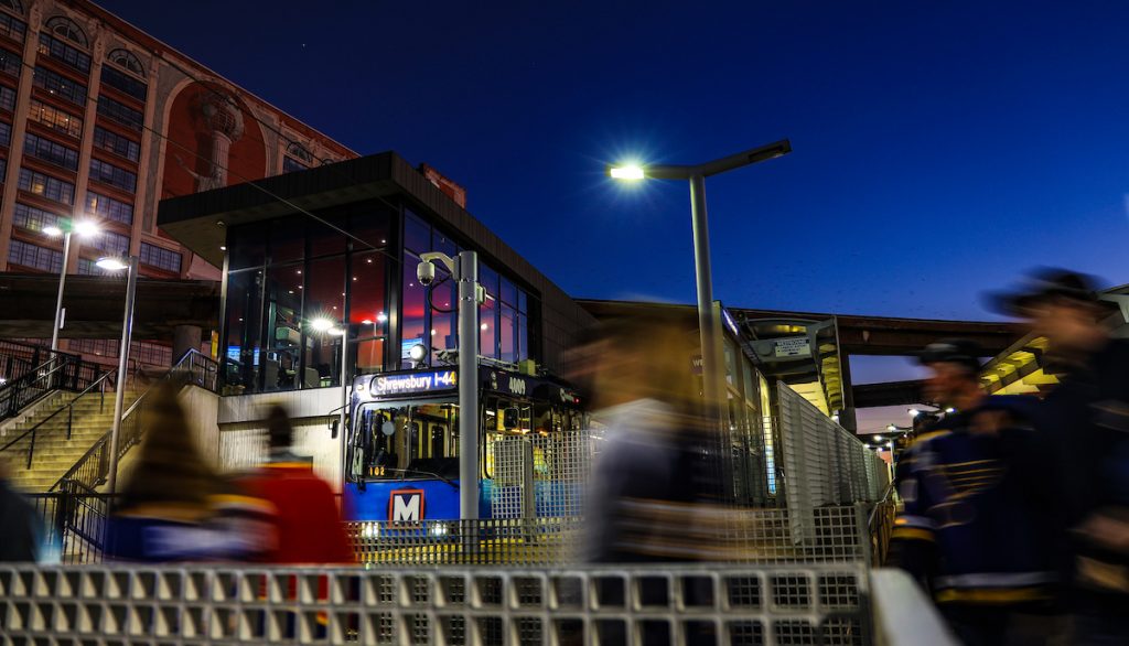 MetroLink train parked at Civic Center Transit Center with riders in St. Louis Blues gear walking across the walkway in front of the train at night