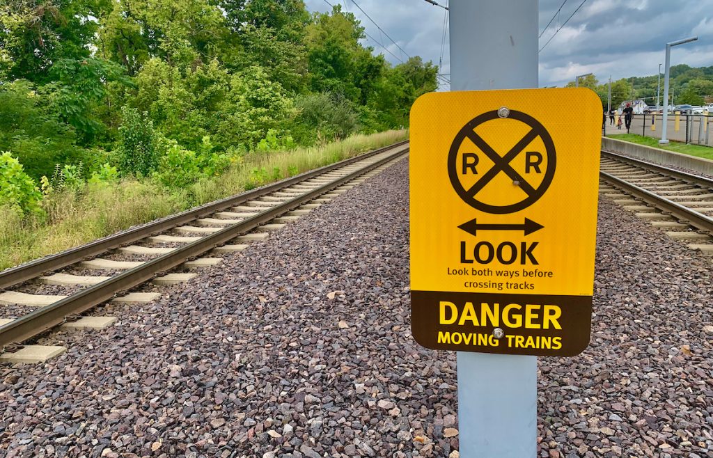 Yellow sign telling people to look both directions and "DANGER Moving Trains" with tracks in the background