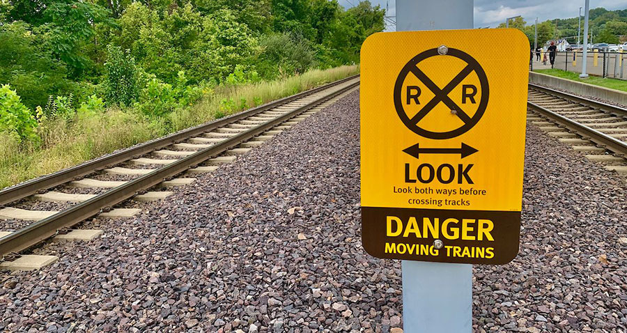 A sign near rail tracks that reads Look both ways before crossing tracks. Danger moving trains.
