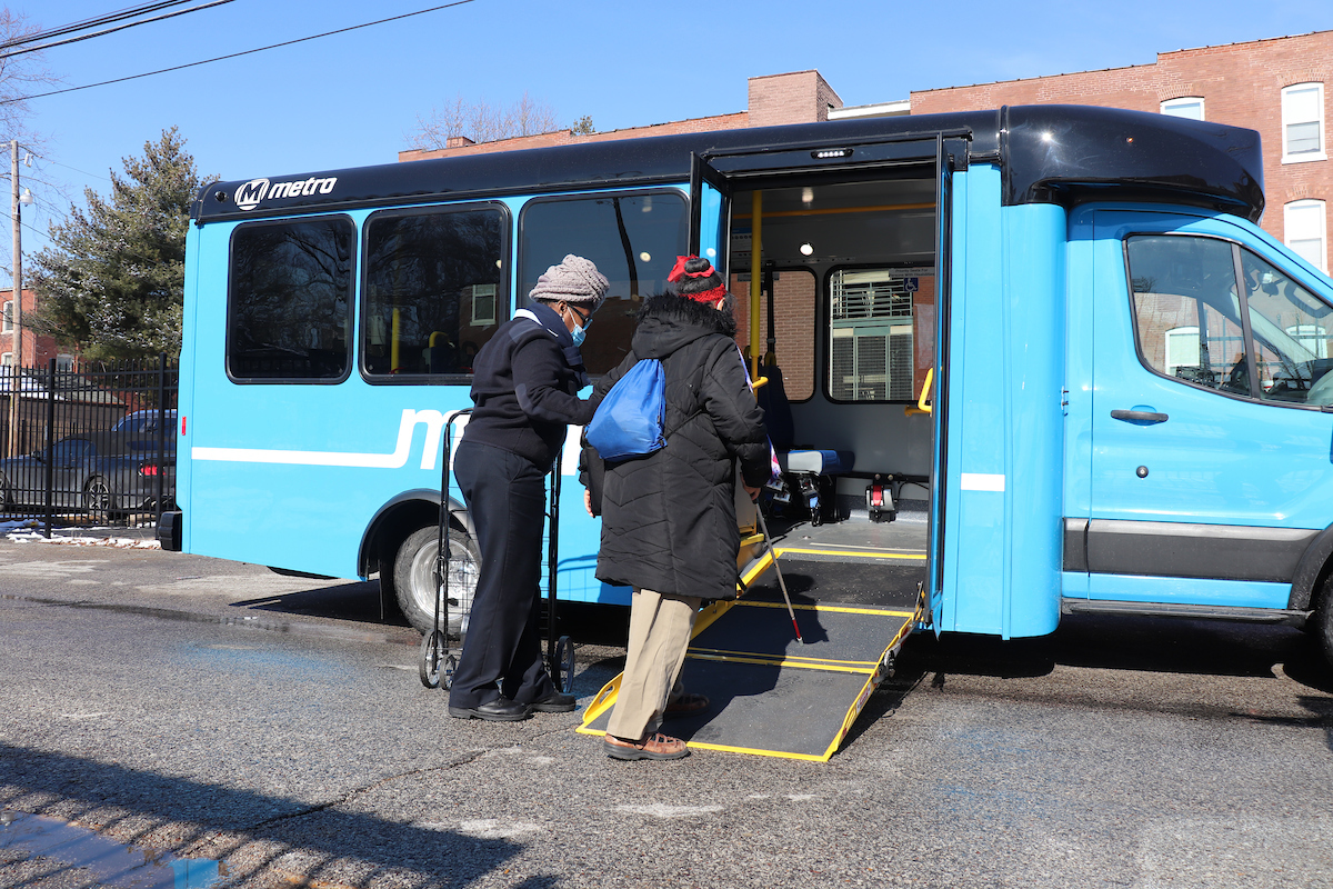 Call-A-Ride operator helps rider to board a Call-A-Ride van. The doors are open and the ramp is lowered.