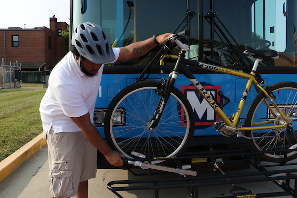 A Transit rider places a bike in the bike rack on the front of a MetroBus.