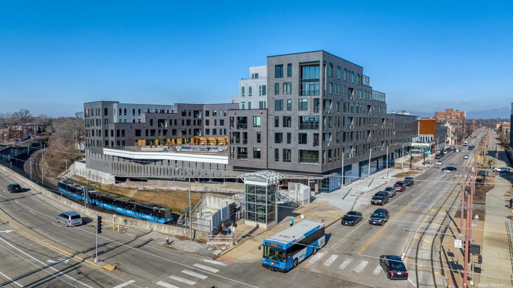 Photo of a MetroLink train and a MetroBus traveling by the Expo at Forest Park mixed-use development