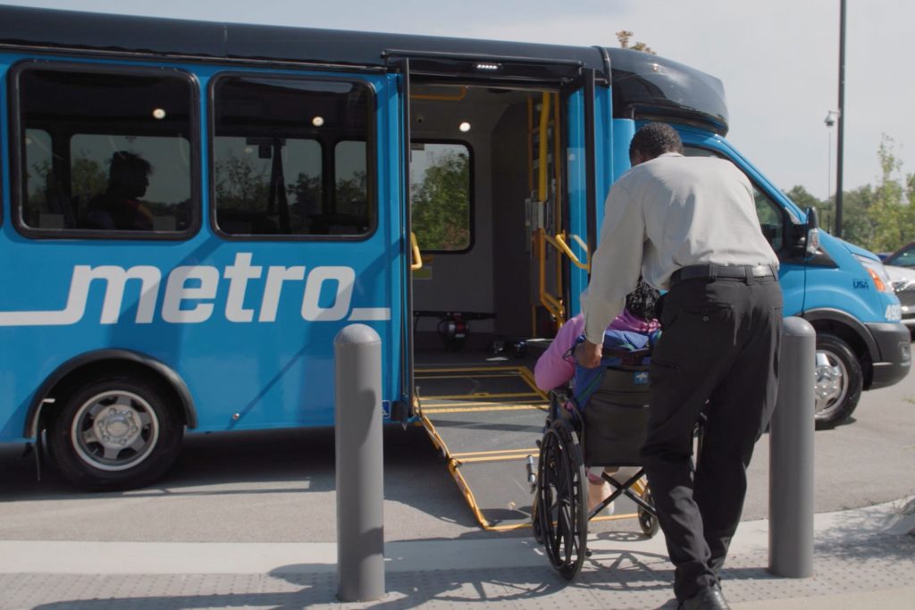 Call-A-Ride operator helps rider to board a Call-A-Ride van. The doors are open and the ramp is lowered.