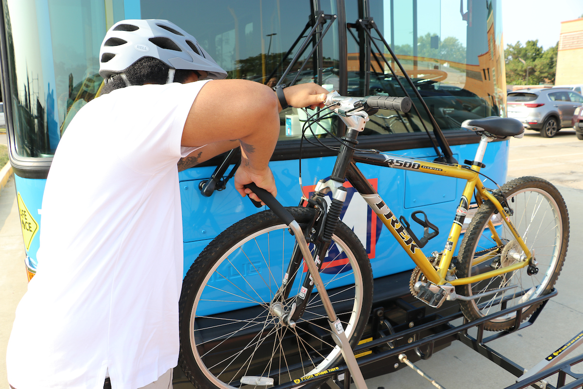 Photo of a cyclist putting their bike on the bike rack attached to the front of a bus