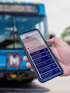 Close-up of MetroBus passenger's hand holding an iPhone with fare options for purchase via app on the screen.