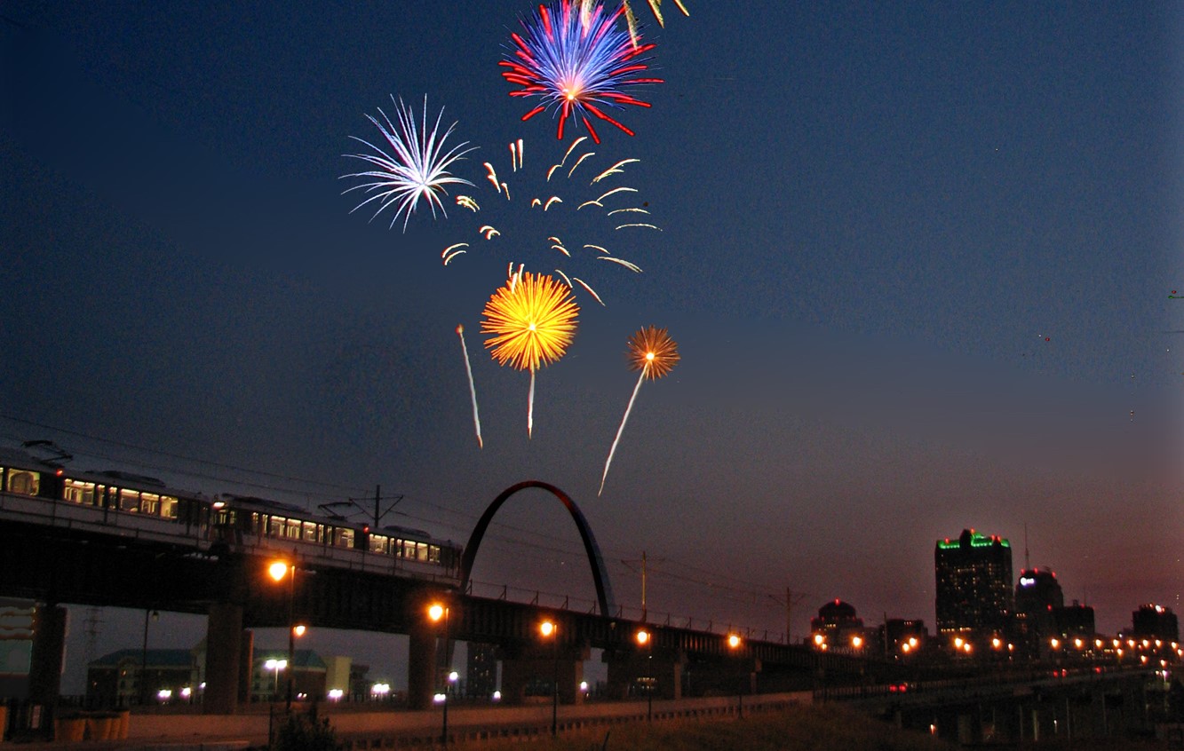 MetroLink crossing Eads Bridge during evening with fireworks in sky above