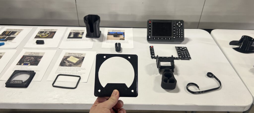 A table covered in a variety of parts that were 3D printed, including a gauge cap cover being held in a hand